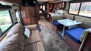 Interior compacto de una caravana con kitchenette, comedor y sala de estar con sofá y cojines.