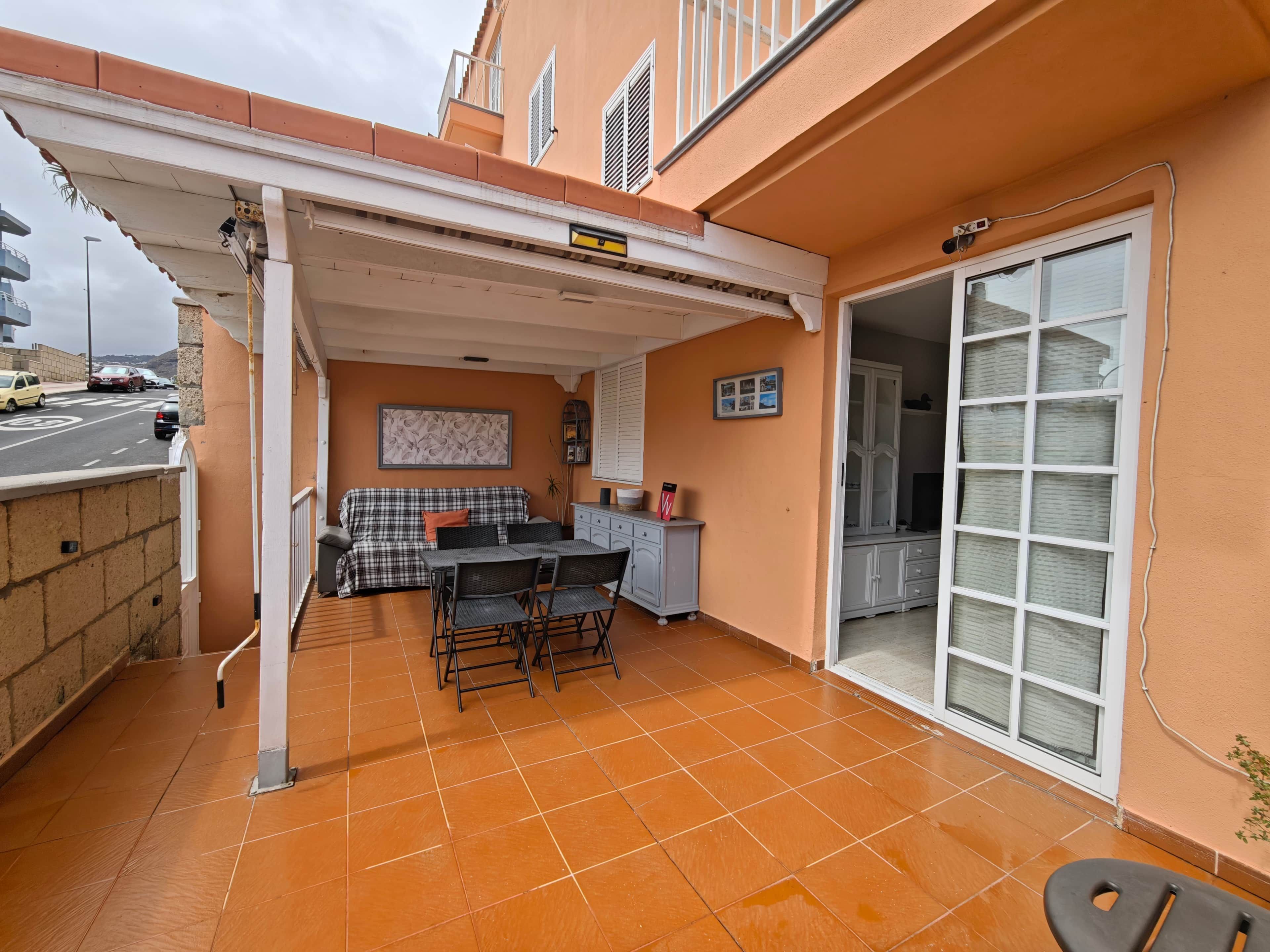 A covered outdoor patio with a dining table and chairs, a sofa, and a sliding glass door leading to an interior room.