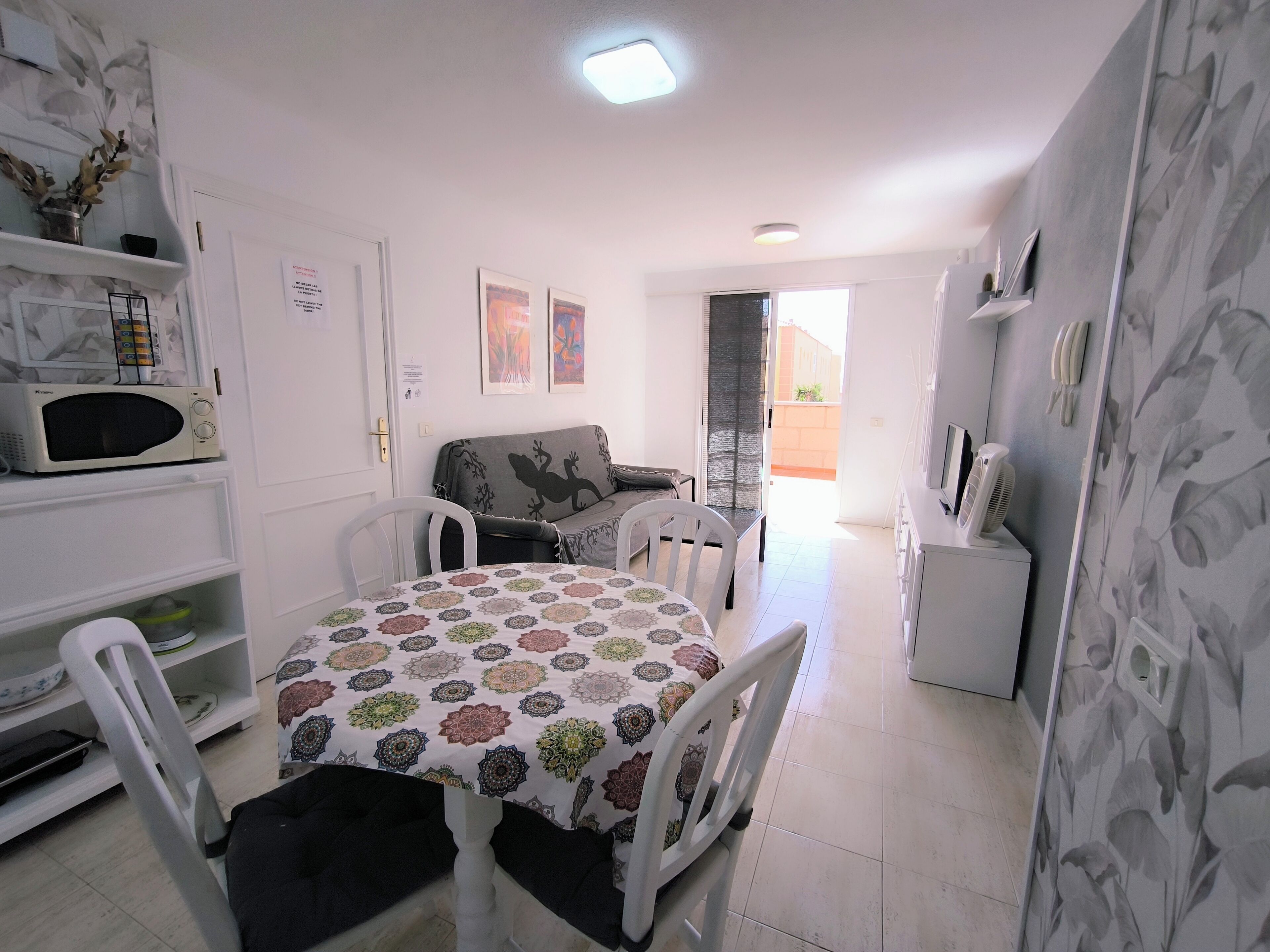 A compact living space with a dining table, chairs, a sofa, a microwave, and a small cabinet.