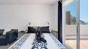 A bedroom with a bed, a sofa, and a view of a mountainous landscape through large windows. - Yinfa Sunset (Tamaimo)