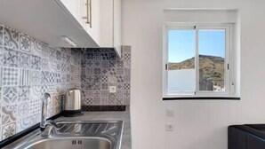 A kitchen with patterned tiles, a stainless steel sink, and a window with a view of hills. - Yinfa Sunset (Tamaimo)