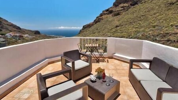 A balcony with a sofa, chairs, and a small table, overlooking a coastal landscape with a clear sky. - Yinfa Sunset (Tamaimo)