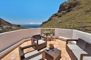A balcony with a sofa, chairs, and a small table, overlooking a coastal landscape with a clear sky. - Yinfa Sunset (Tamaimo)