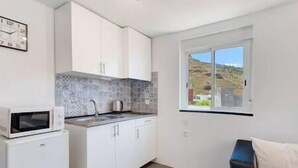 A compact kitchen with white cabinets, a microwave, and a window with a view of a hilly landscape. - Yinfa Sunset (Tamaimo)