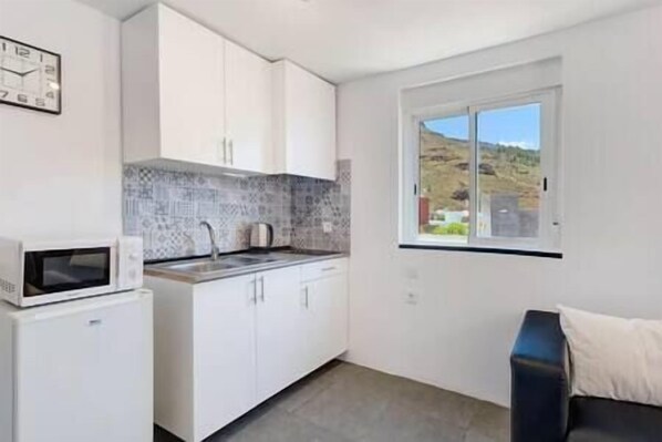 A compact kitchen with white cabinets, a microwave, and a window with a view of a hilly landscape. - Yinfa Sunset (Tamaimo)