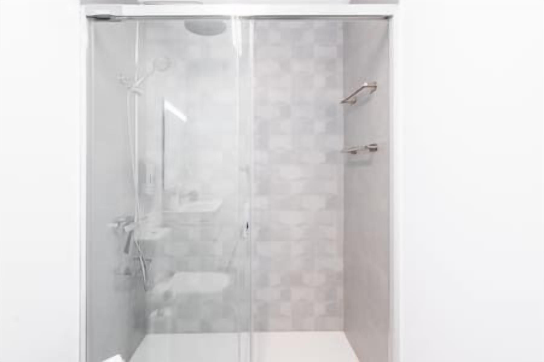 Une douche fermée par des parois en verre, avec un mur carrelé et un sol blanc.
