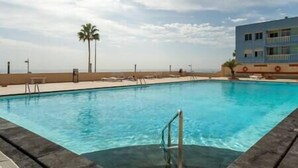 A swimming pool with a clear view of the ocean and a building in the background. - Susurros of the sea Apartment (Candelaria)