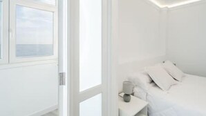 A white room with a bed, a nightstand, and a window with a view of the sea. - Susurros of the sea Apartment (Candelaria)