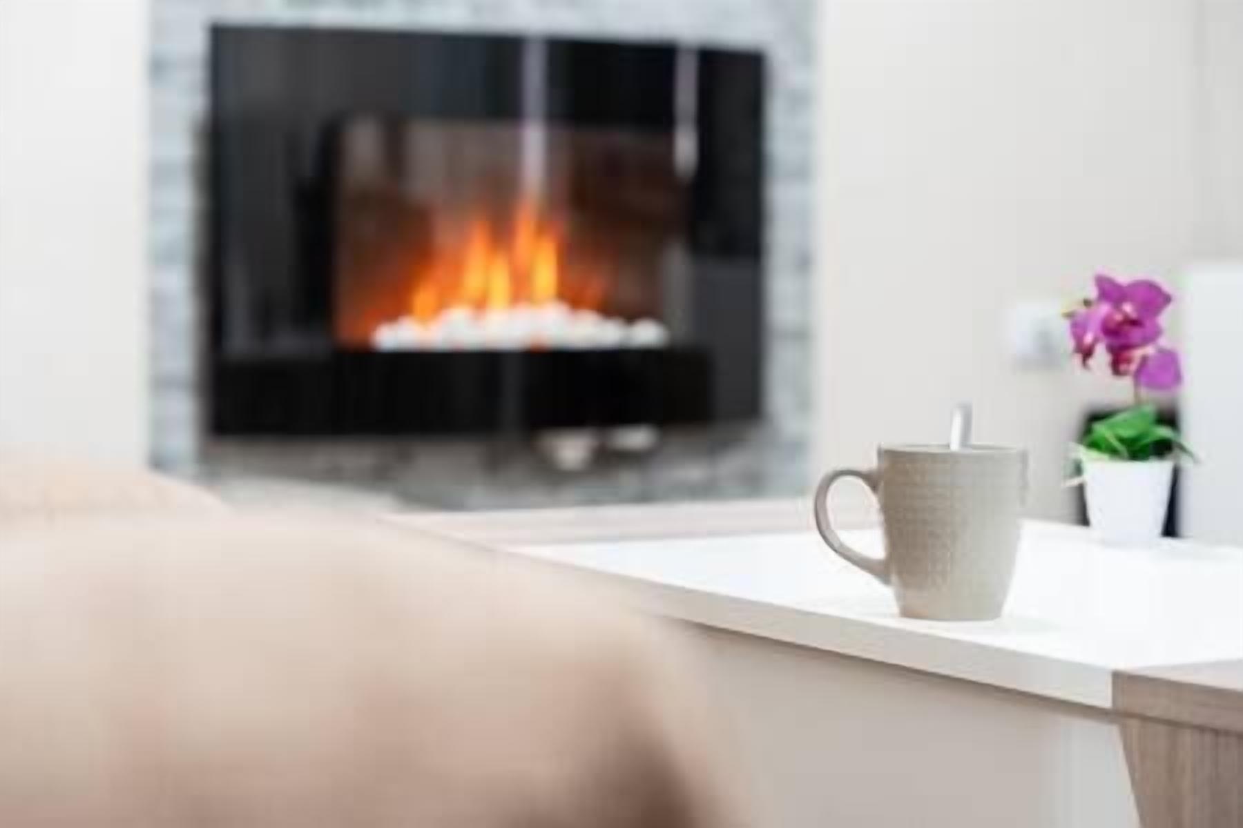 A cozy living room with a fireplace, a coffee mug on a table, and a potted orchid.