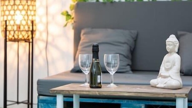 A table with a bottle and two glasses, a white Buddha statue, and a grey sofa with cushions. - Branmi House Big Ravine (Santa Cruz de Tenerife)
