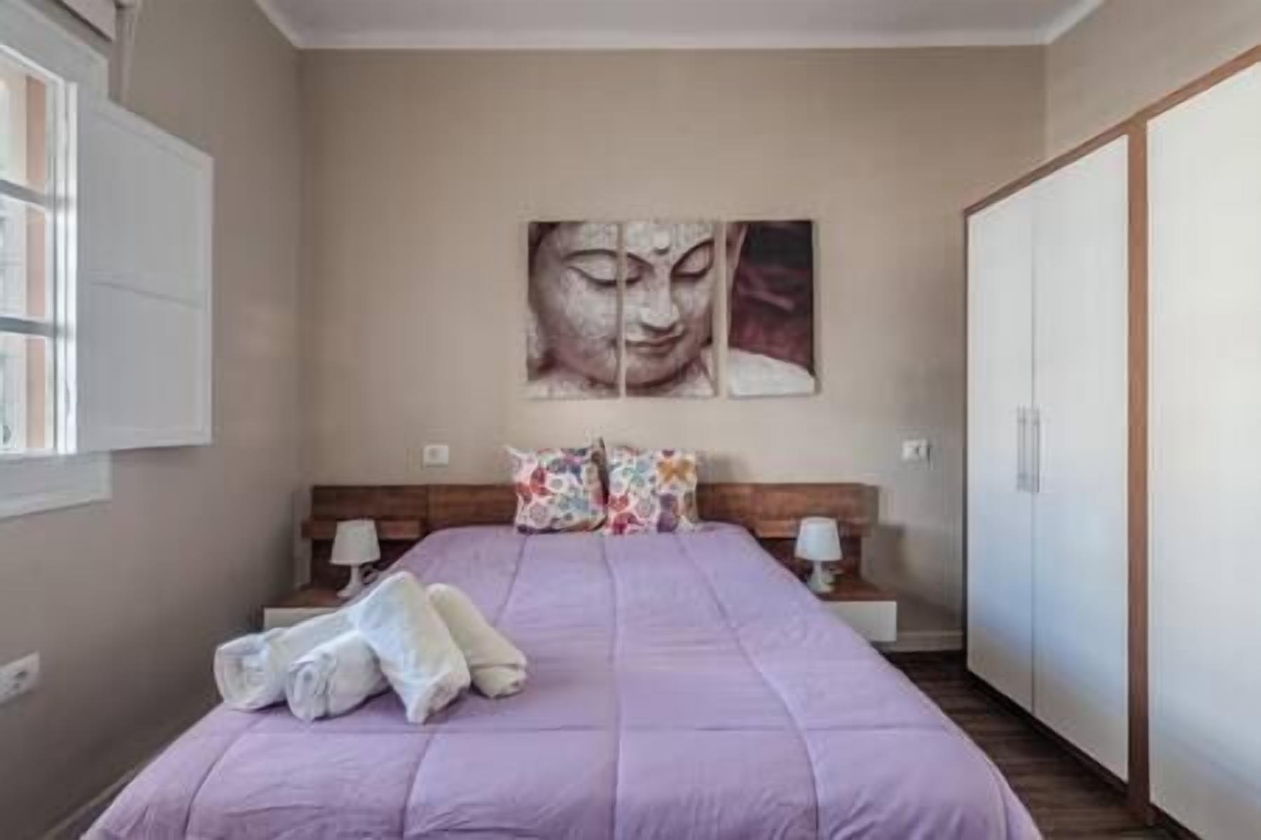 A bedroom with a bed, pillows, a nightstand, a wall-mounted painting, and a wardrobe.