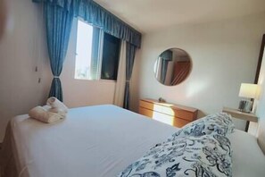 Une chambre d’hôtel avec un lit, une commode, un miroir et une lampe.