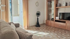 En stue med sofa, ventilator, fjernsyn og skab.