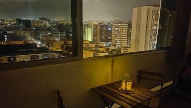 En balkon med et bord og stole, der udover en bygnings silhuet i nattens mørke.