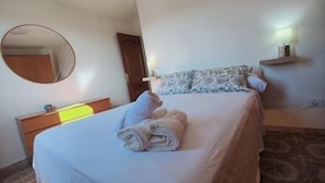 Et hotelværelse med en seng, et rundt spejl, et sengebord og en hylde på væggen.