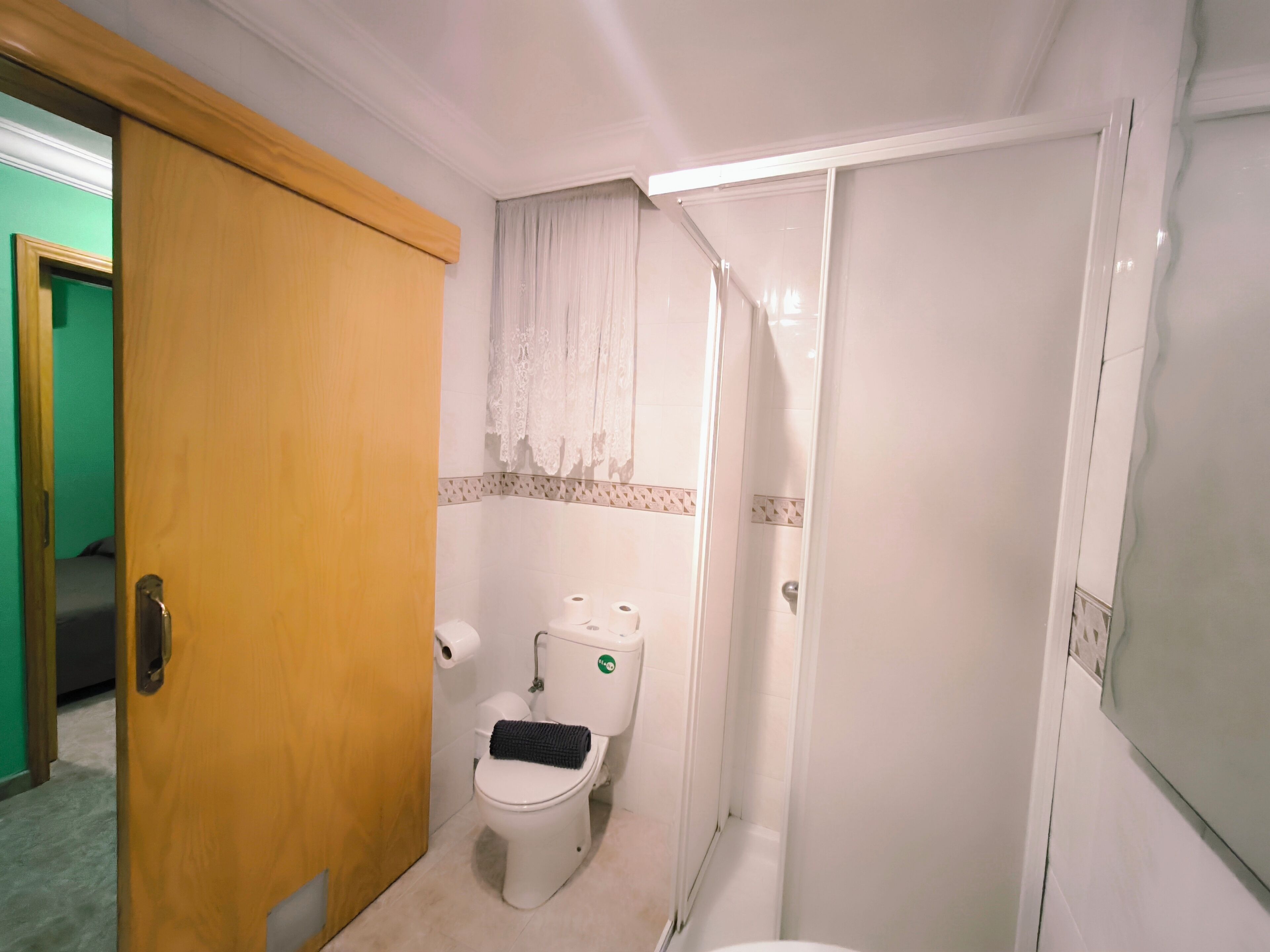 A small bathroom with a toilet, a shower, and a wooden door.