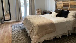 A bedroom with a large bed, a wooden headboard, a nightstand, a chair, a mirror, and a window with curtains. - Warm welcoming stay (Mandeville)