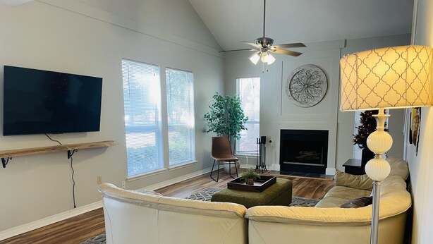 A living room with a sectional sofa, a flat-screen TV, a fireplace, and a ceiling fan. - Warm welcoming stay (Mandeville)