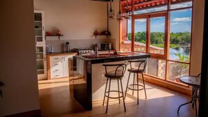 A kitchen with a large island, bar stools, and a view of a river through large windows.