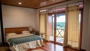 A bedroom with a wooden ceiling, a bed with a green and white bedspread, a small round rug, and a view of a wooden deck through a glass door.