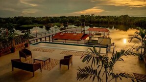 A pool area with lounge chairs and a view of a lake at sunset.