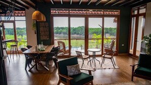 A spacious room with a wooden dining table, chairs, and a view of a lush green landscape through large sliding doors.
