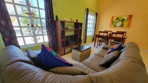 A living room with a large L-shaped sofa, a small TV stand, a bookshelf, and a dining area with chairs. - Condo on the Caribbean (Isla Mujeres)