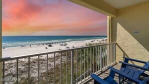Een balkon met uitzicht op een strand en de oceaan tijdens zonsondergang.