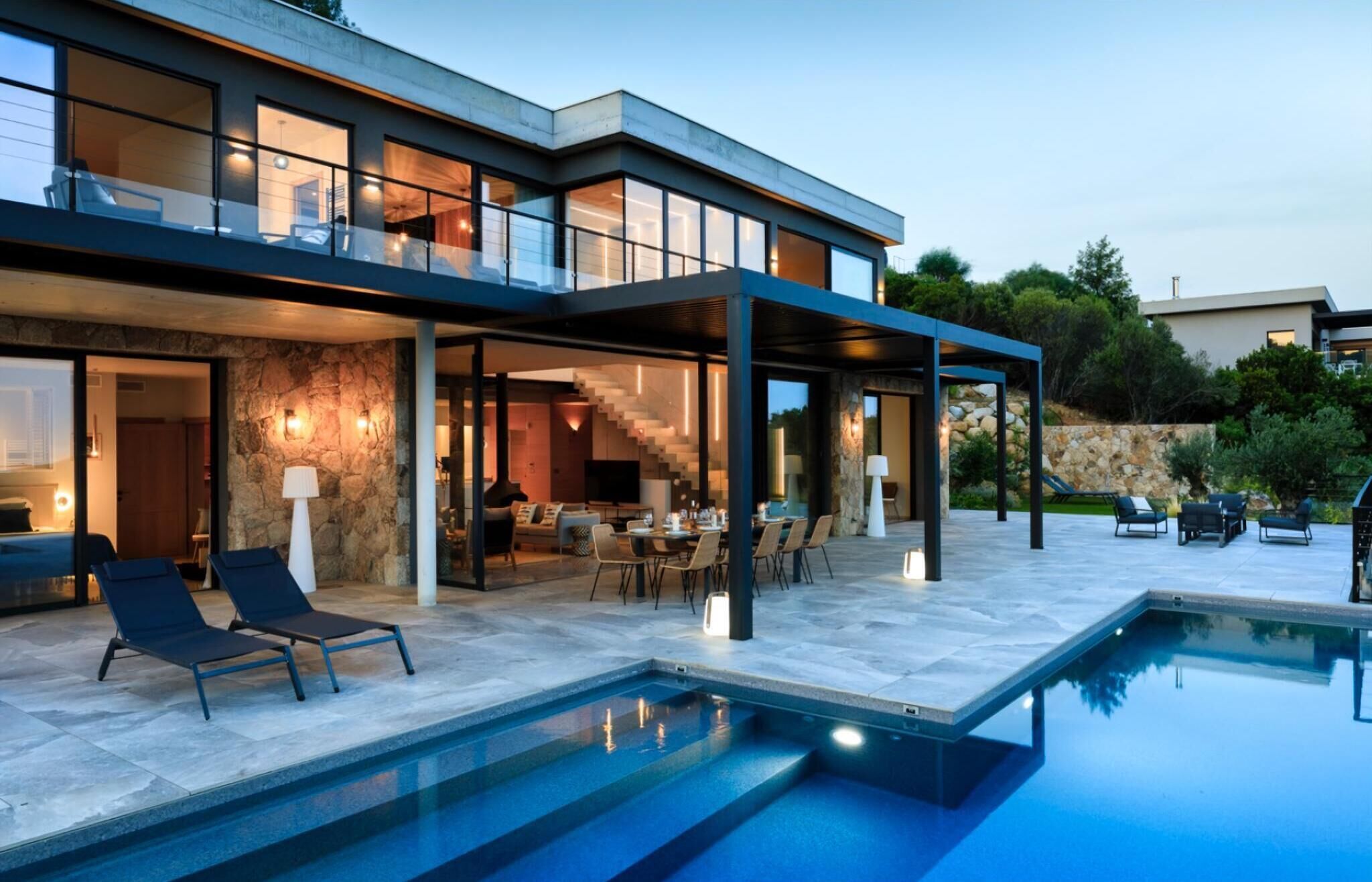 Une maison moderne dotée d’une piscine, d’un espace salon extérieur et d’un mur en pierre.