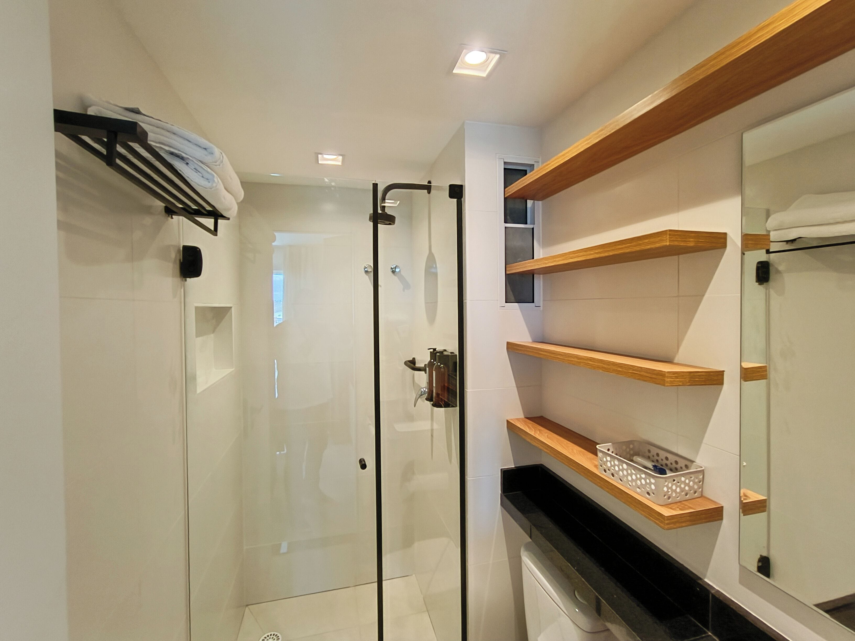A modern bathroom with a glass shower enclosure, wooden shelves, and a large mirror.