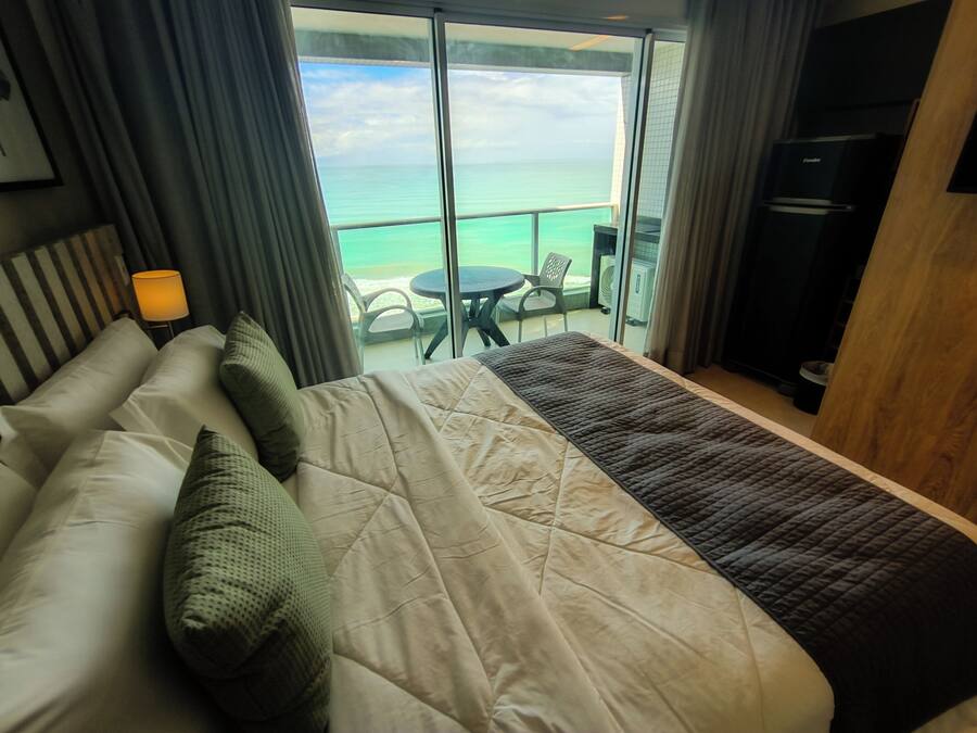 A hotel room with a bed, a table, and a view of the ocean.