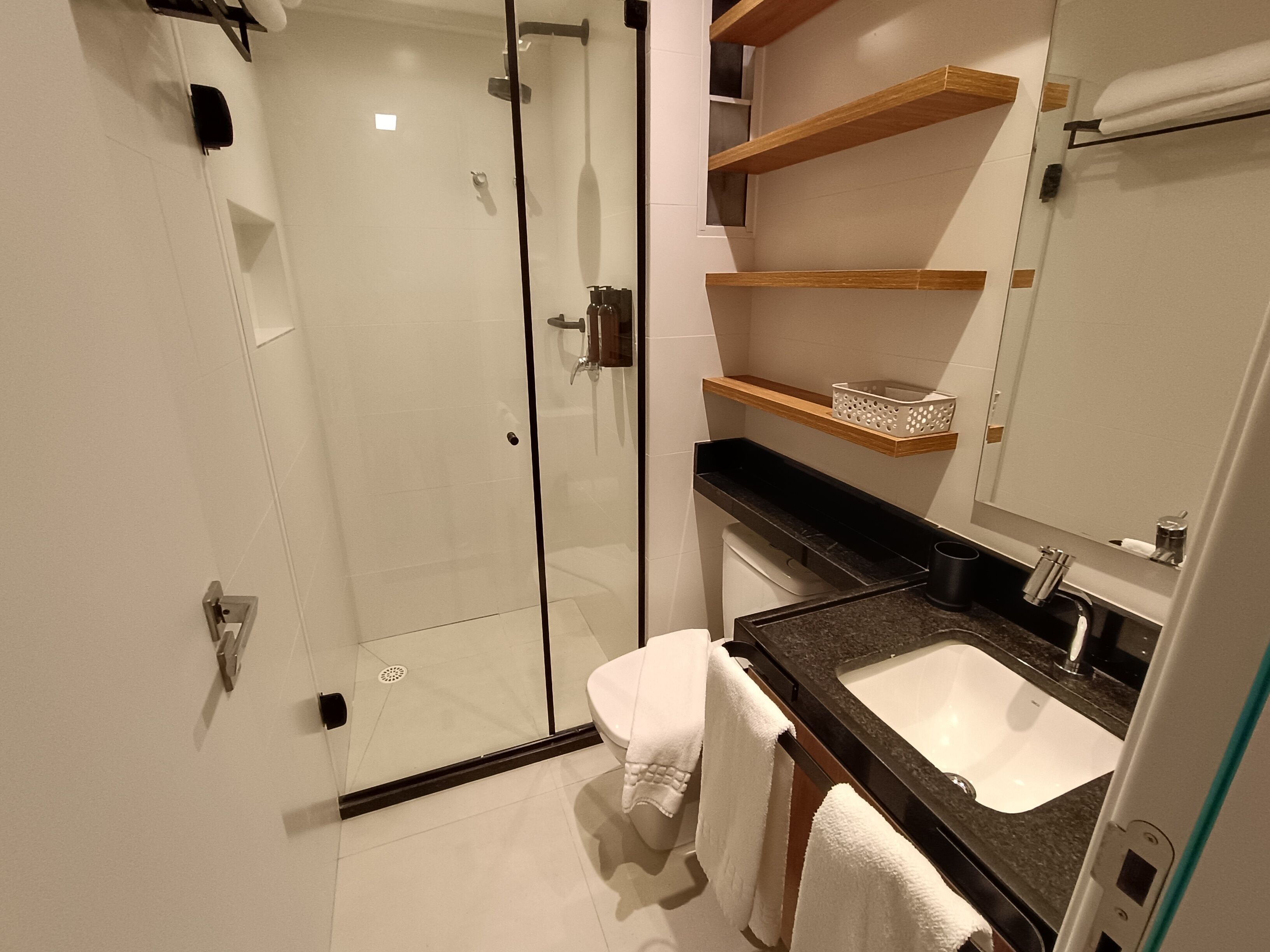 Un baño moderno con cabina de ducha de vidrio, un lavamanos blanco y estantes de madera sobre el mostrador.
