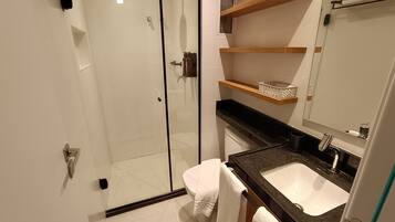 Un baño moderno con cabina de ducha de vidrio, un lavamanos blanco y estantes de madera sobre el mostrador.