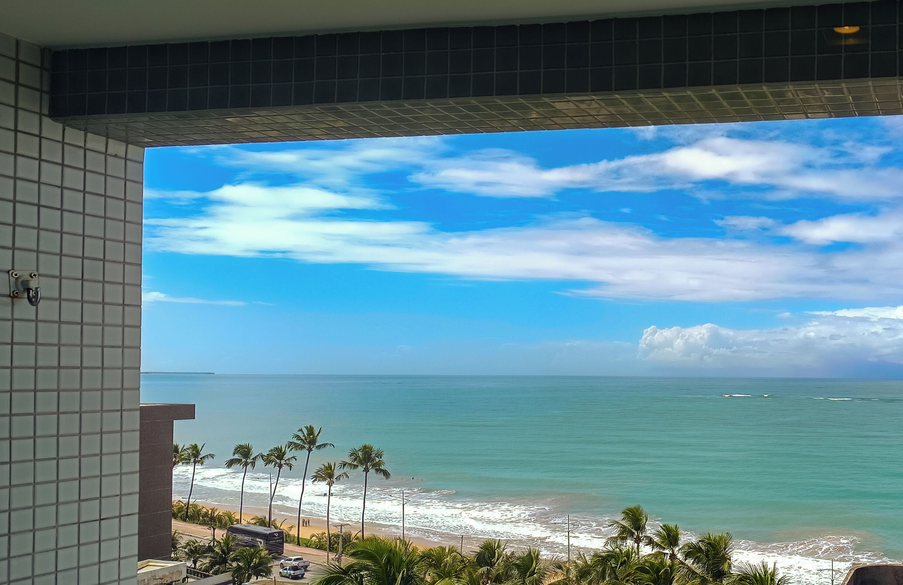 A view from a balcony overlooking a beach with palm trees and a clear sky.