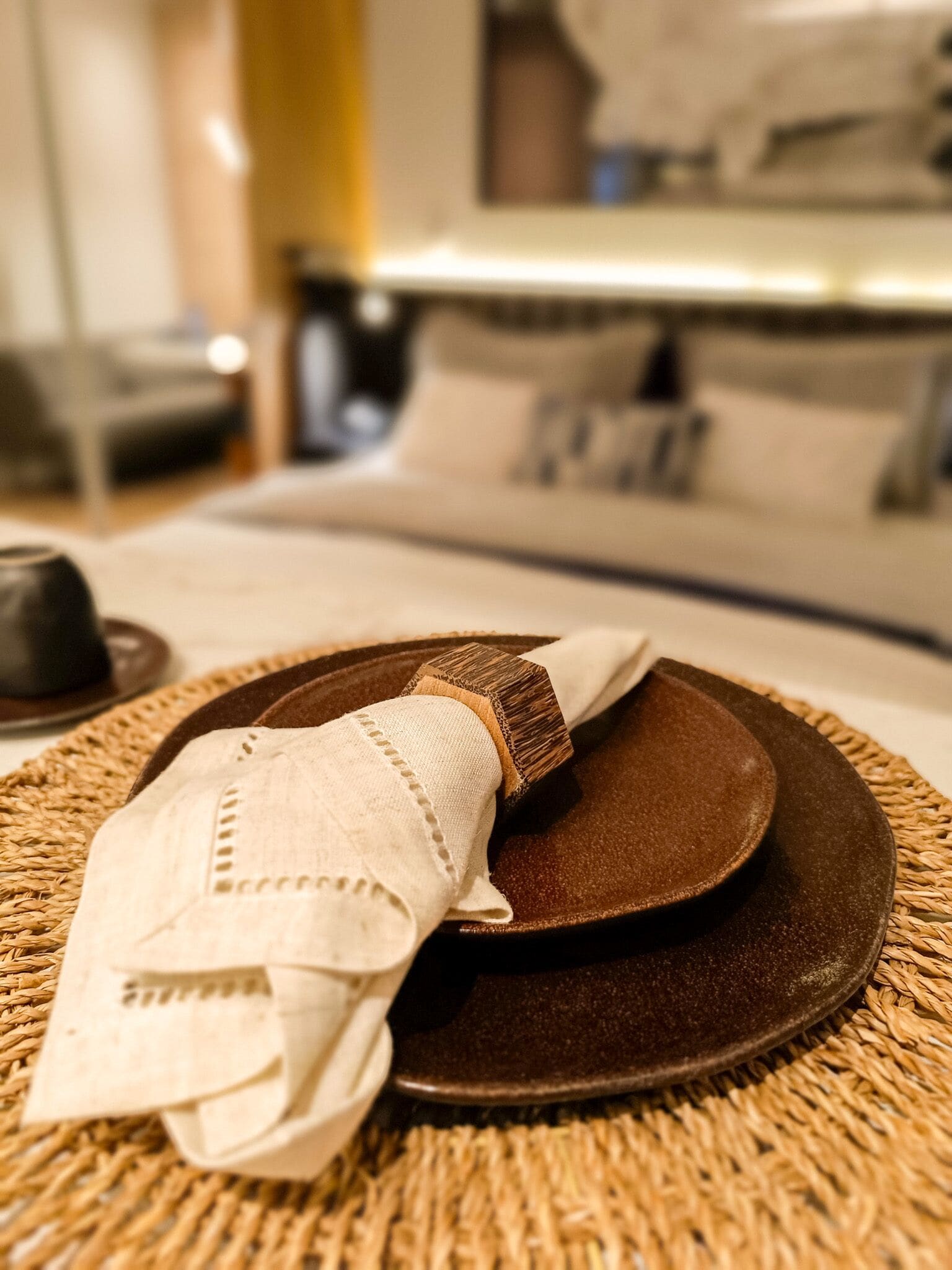 A neatly arranged dining setup with a plate, napkin, and a woven placemat on a bed.
