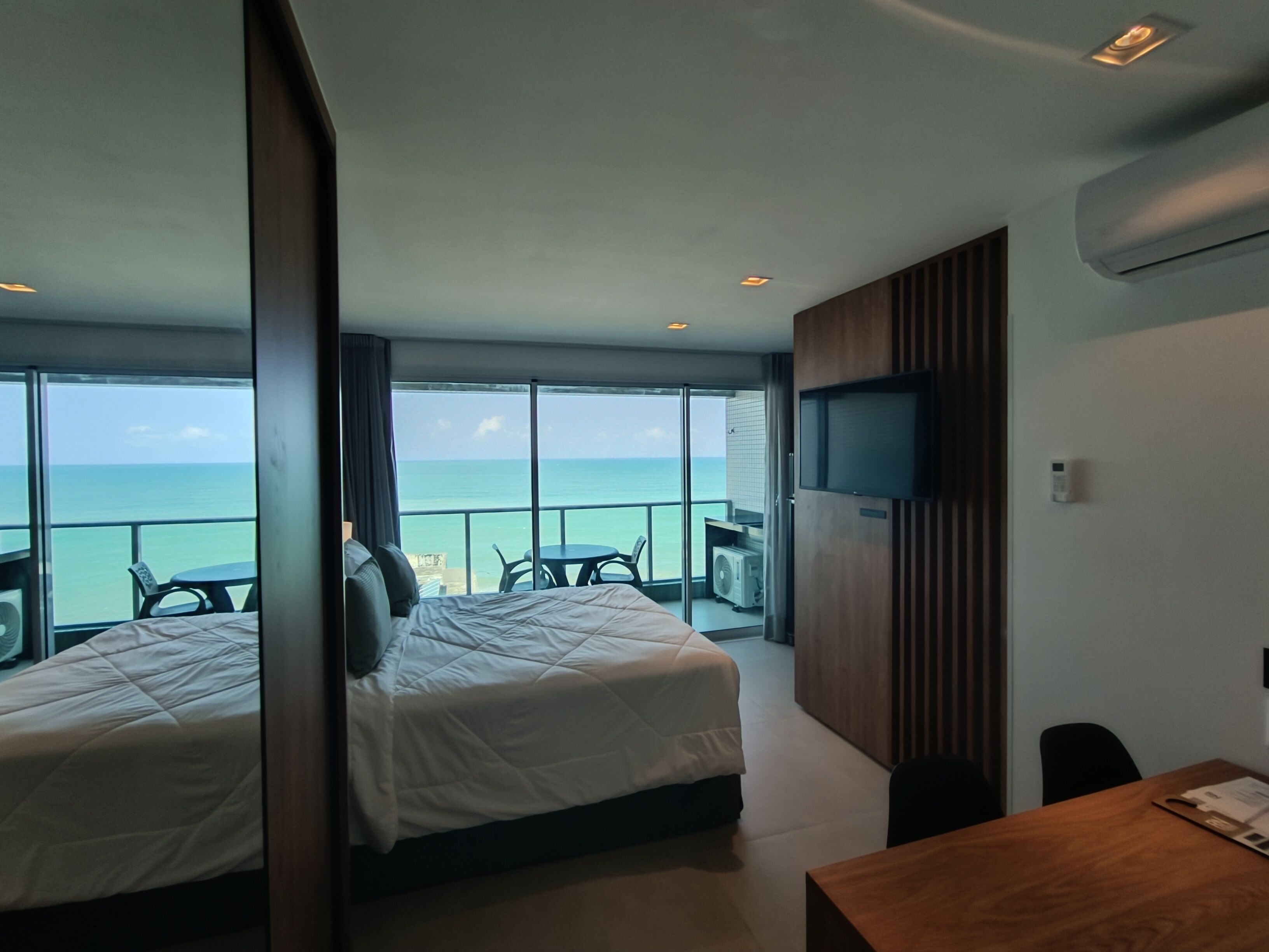 Ein Hotelzimmer mit zwei Betten, einem Fernseher und einem Balkon mit Meerblick.