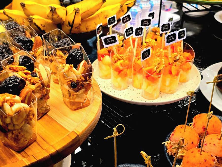 Buffet com diversos alimentos, incluindo frutas, sobremesas e petiscos.