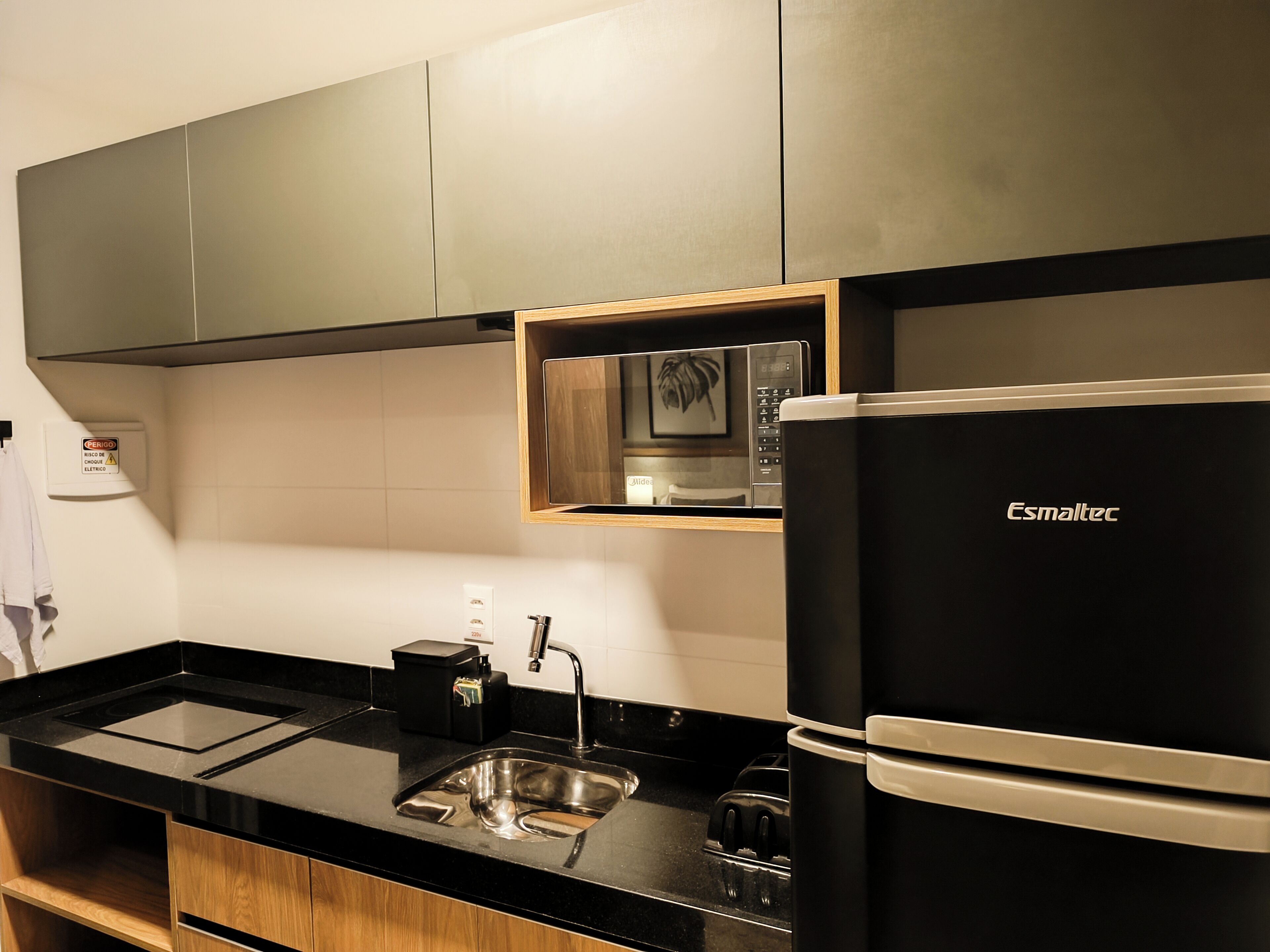 A modern kitchen with a black Esmaltec refrigerator, a built-in microwave, and a stainless steel sink.
