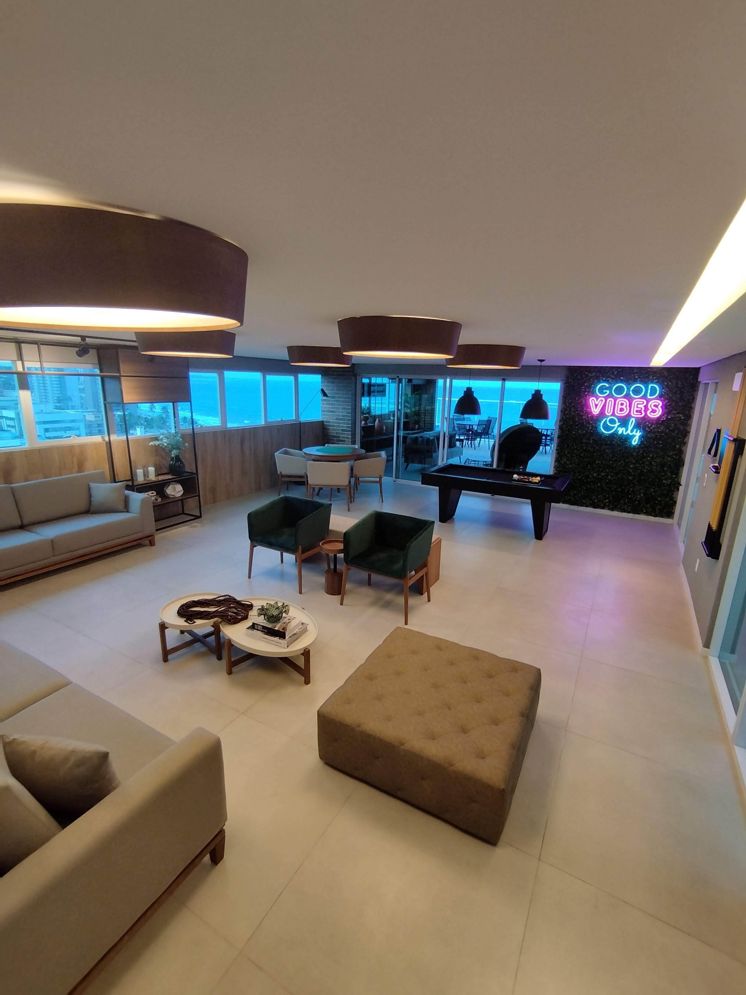 Una sala de estar moderna con mesa de billar, asientos cómodos y un letrero de neón que dice "GOOD VIBES Only".