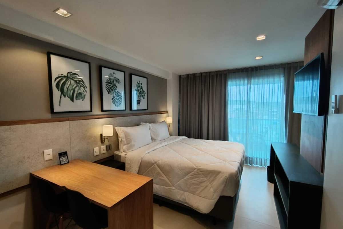 A hotel room with a bed, a desk, a chair, a TV, and framed artwork on the wall.