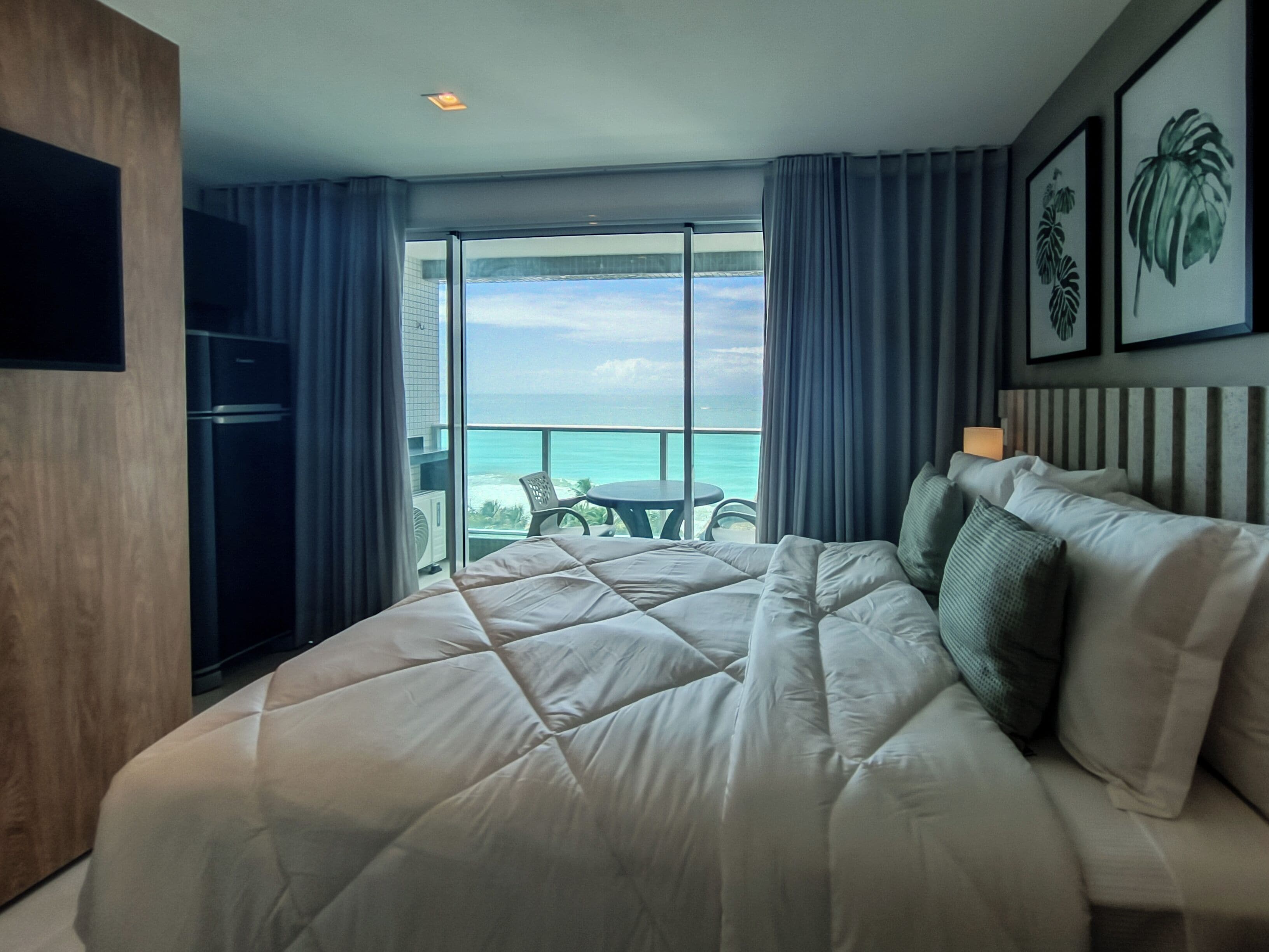 Ein Hotelzimmer mit einem großen Bett, einem Fernseher, einem Balkon mit Meerblick und einem Essbereich.