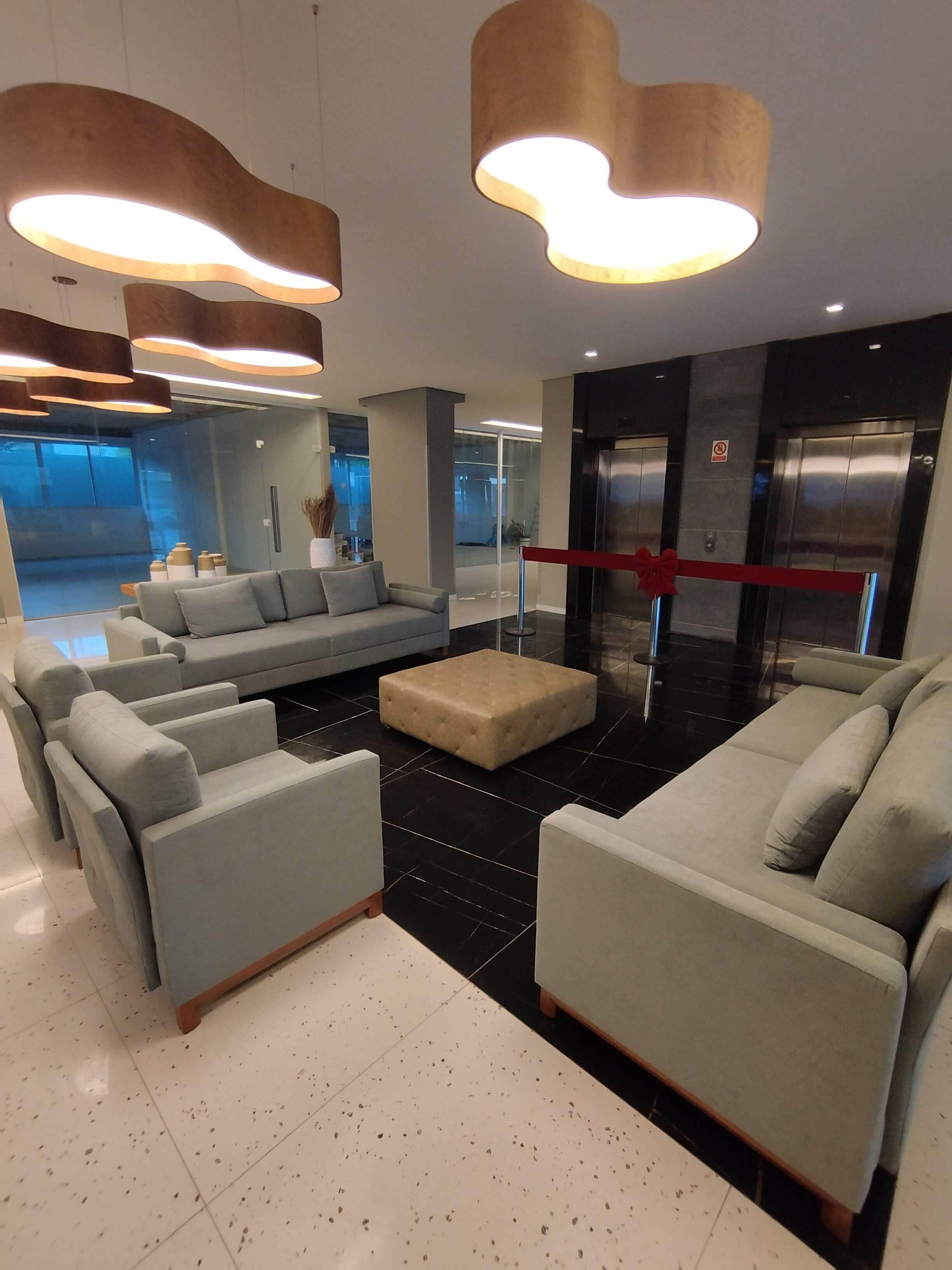 A modern lobby with a grey sofa set, a tufted ottoman, and a red barrier near elevators.