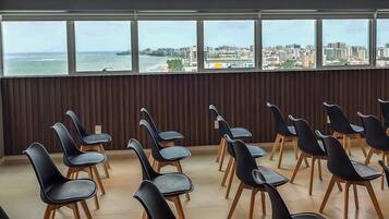 Un salón de conferencias con filas de sillas negras de patas de madera, ventanas amplias con vista a la ciudad y un panel de pared de madera.