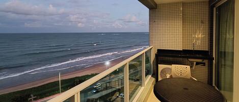 A balcony with a view of the ocean, a table, and a chair.