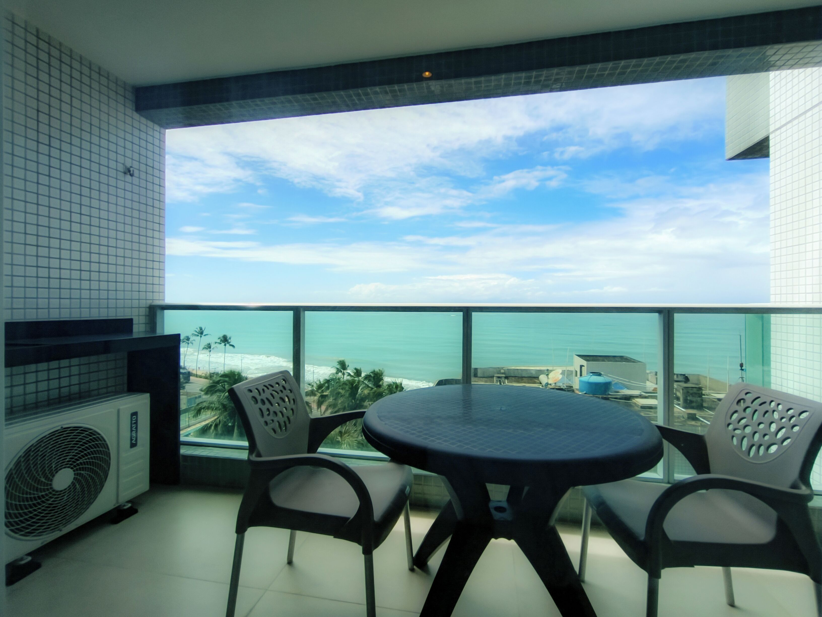 A balcony with a round table and four chairs, overlooking a beach and ocean.