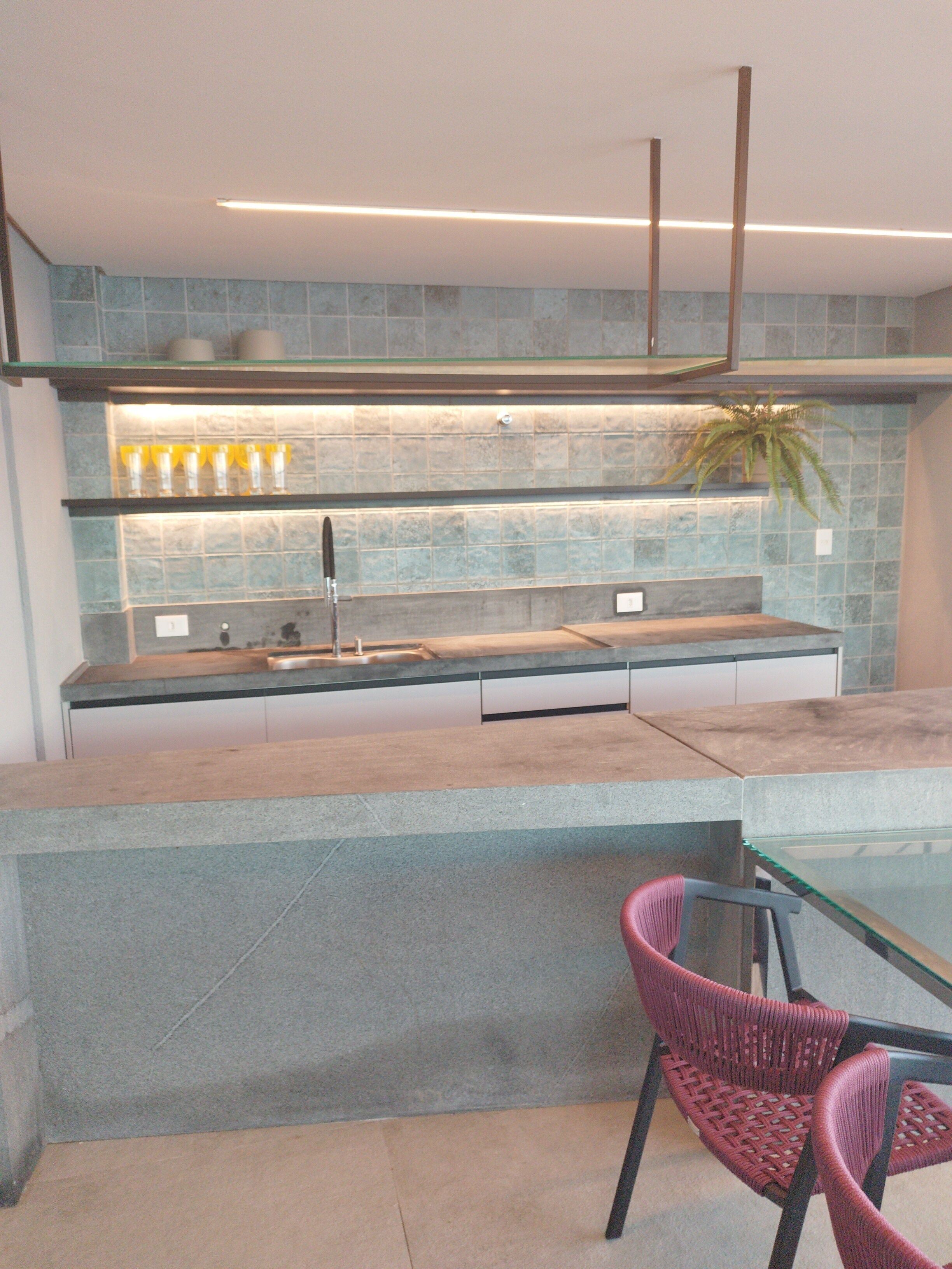 A modern kitchen with a central island, a sink, and a glass-top dining table with chairs.