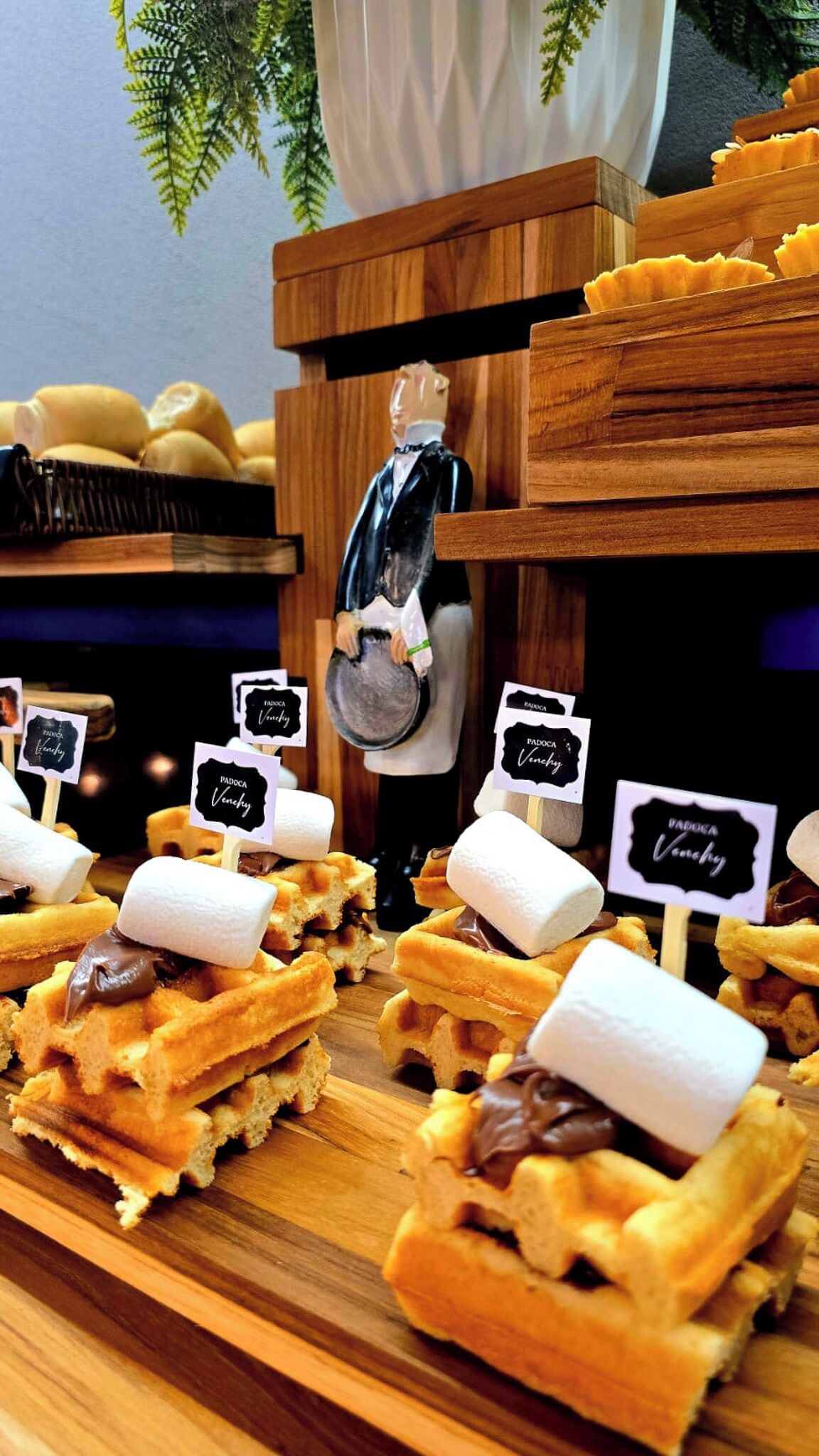 A display of mini waffles with marshmallows and chocolate on a wooden table.