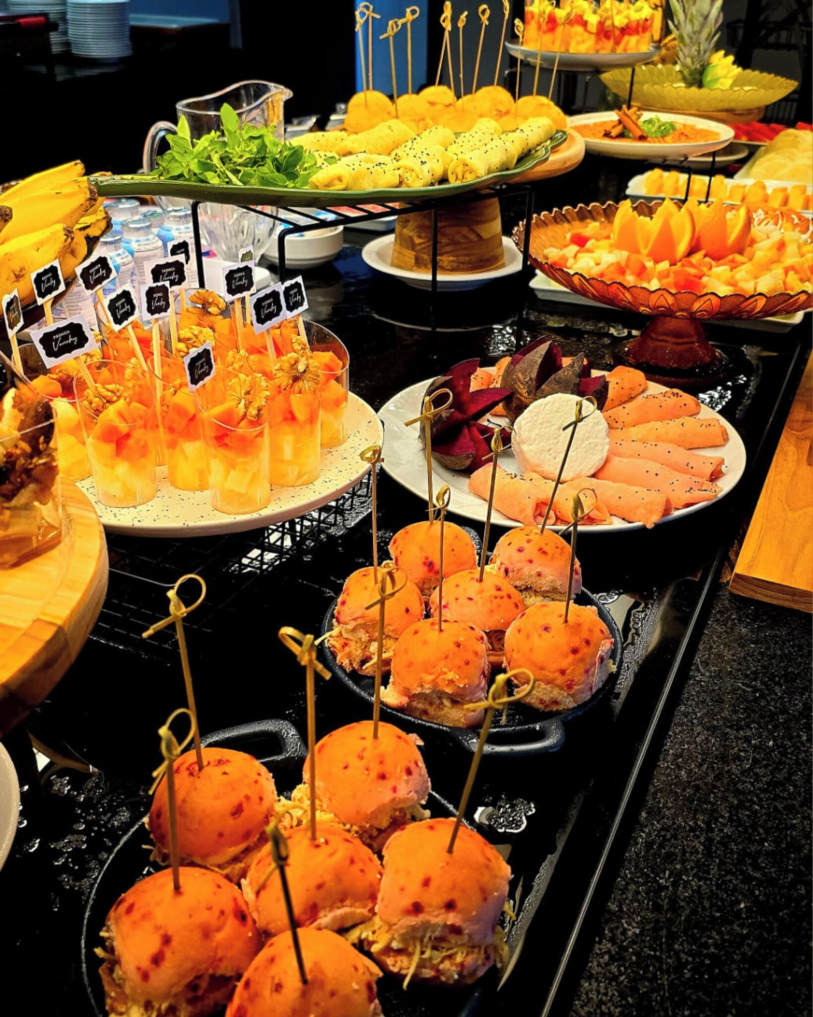 A buffet with various food items including fruit skewers, a dish with a pineapple, and a plate with what appears to be a seafood dish.