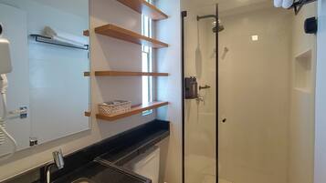 A modern bathroom with a glass shower enclosure, a sink with a black countertop, and wooden shelves above the mirror.