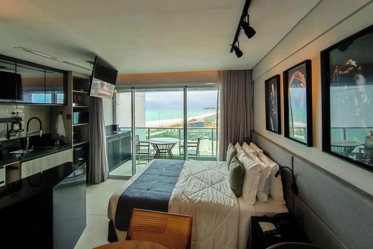 A modern hotel room with a balcony, a bed, a desk, and a TV.